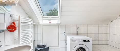 A modern bathroom with a skylight, a washing machine, a bathtub, and a large mirror.