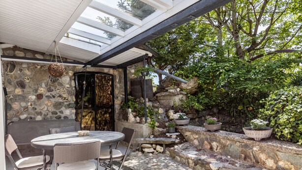 An outdoor patio with a stone wall, a round table, wicker chairs, and potted plants.