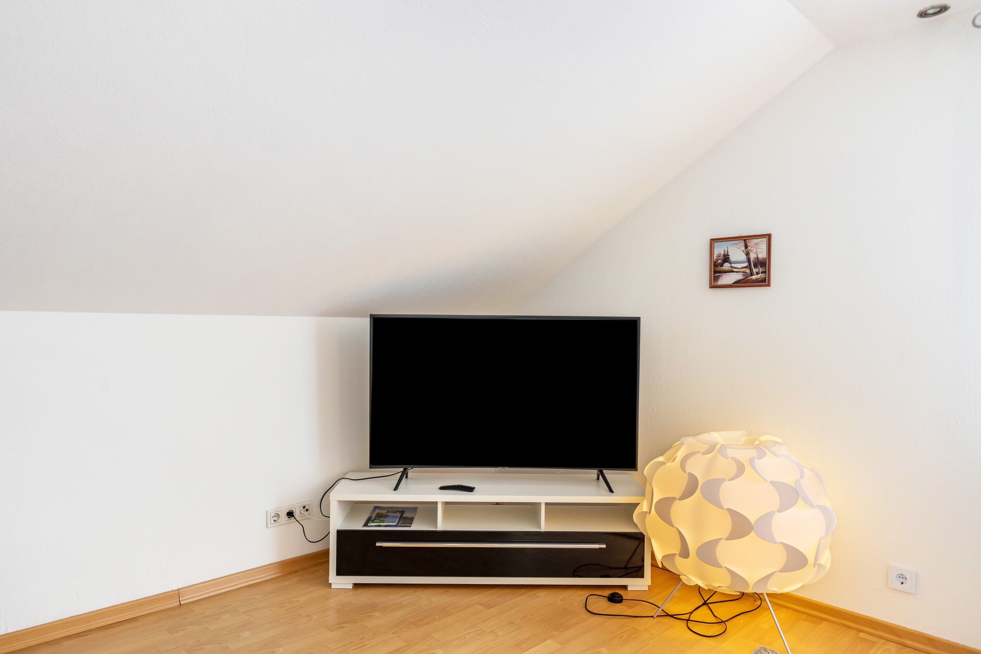 A modern living room with a flat-screen TV on a white entertainment unit, a spherical lamp, and a small framed picture on the wall.