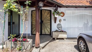A building with a tiled roof, a large wooden door with a sunburst design, and a small stone statue on a bench.