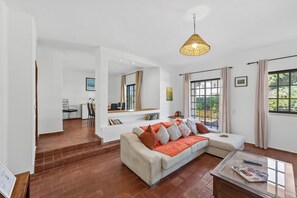 Ein modernes Wohnzimmer mit einer Eckcouch, einem Glastisch und einem großen Fenster mit Vorhängen.
