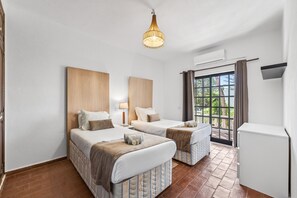 Ein Hotelzimmer mit zwei Betten, einem Kronleuchter, einem Fenster mit Vorhängen und einem weißen Schrank.