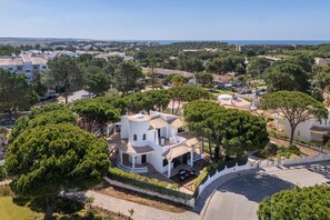 Eine weiße Villa mit gewundener Dachform, umgeben von viel Grün und einer gepflasterten Auffahrt.