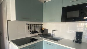 A kitchen with light blue cabinets, a black stove, and a coffee maker. - Charming and cosy T2 near the beach, parking space (Sète)