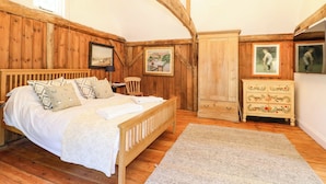 A bedroom with a wooden bed, a dresser, a chair, and a painting on the wall. - The Granary (Petworth)
