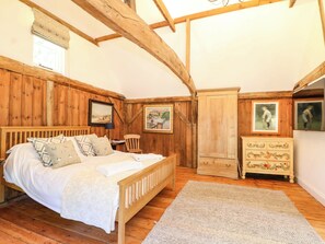 A bedroom with a wooden bed, a dresser, a chair, and a painting on the wall. - The Granary (Petworth)