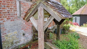 A rustic wooden structure with a sloped roof, a brick wall, and a garden area with plants and gravel. - The Granary (Petworth)