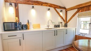 A kitchen with white cabinets, wooden beams, a microwave, and a sink. - The Granary (Petworth)