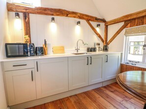 A kitchen with white cabinets, wooden beams, a microwave, and a sink. - The Granary (Petworth)