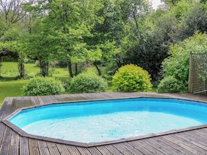 A rectangular swimming pool with a wooden deck, surrounded by lush greenery and trees. - The Granary (Petworth)