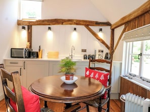A kitchen with a wooden table, chairs, a microwave, and a window with a view. - The Granary (Petworth)