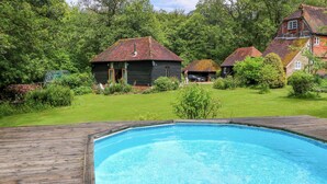A swimming pool with a wooden deck, surrounded by a grassy lawn and houses with red-tiled roofs. - The Granary (Petworth)
