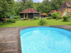 A swimming pool with a wooden deck, surrounded by a grassy lawn and houses with red-tiled roofs. - The Granary (Petworth)