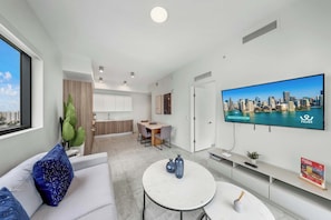 A modern living room with a flat-screen TV, a dining area, and a kitchen in the background. - Luxe 1BR Balcony • Near FIFA Fan Fest (Miami)