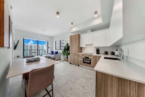A modern kitchen with a dining area, large windows, and a view of buildings. - Luxe 1BR Balcony • Near FIFA Fan Fest (Miami)