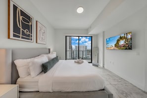 A modern hotel room with a large bed, a television, and a view of the cityscape. - Luxe 1BR Balcony • Near FIFA Fan Fest (Miami)