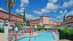 Un espace piscine comprenant plusieurs bassins, entouré d’une clôture, avec en arrière-plan des bâtiments aux toits recouverts de tuiles rouges.