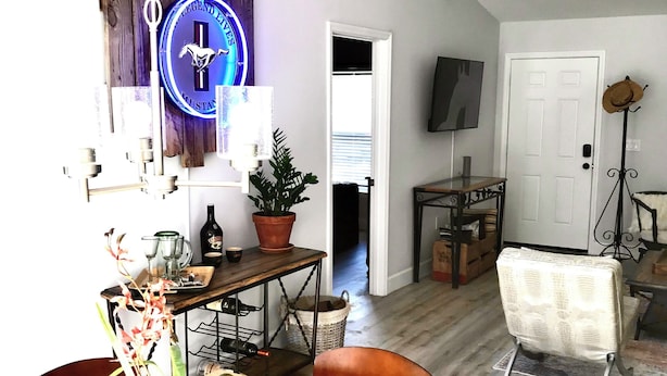 Ein Essbereich mit Holztisch, Stühlen und einem Blumentopf. Ein an der Wand befestigter Fernseher und eine Tür zu einem anderen Raum sind ebenfalls vorhanden.