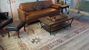 Ein Wohnzimmer mit braunem Ledersofa, einem Holztisch, einem gemusterten Teppich und einem schwarzen Ledersessel.