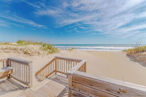 Ein hölzerner Steg führt zu einem Strand mit Dünen und Meerblick.