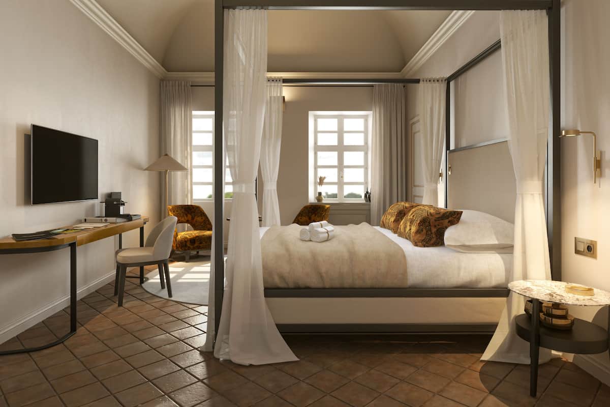 A four-poster bed with white curtains, a desk with a flat-screen TV, a chair, and a bedside table with a lamp.