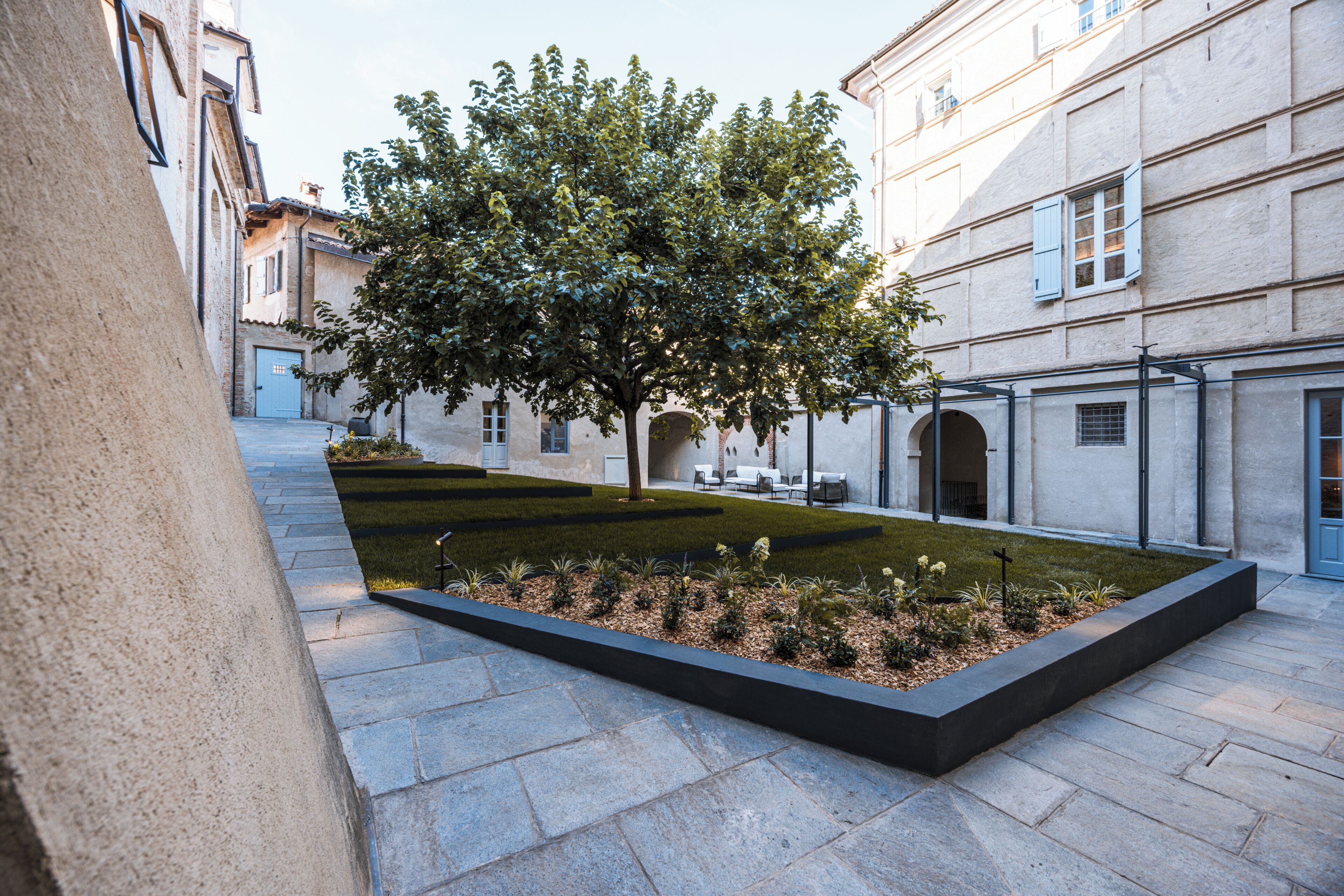 A courtyard with a tree, a seating area, and a building with a door and windows.