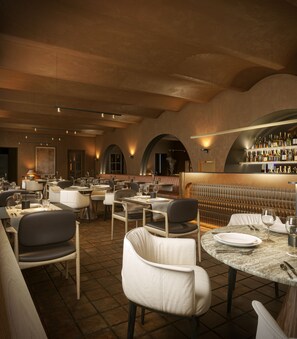 En restaurantindretning med borde, stole, en bar og et højt til loftet.
