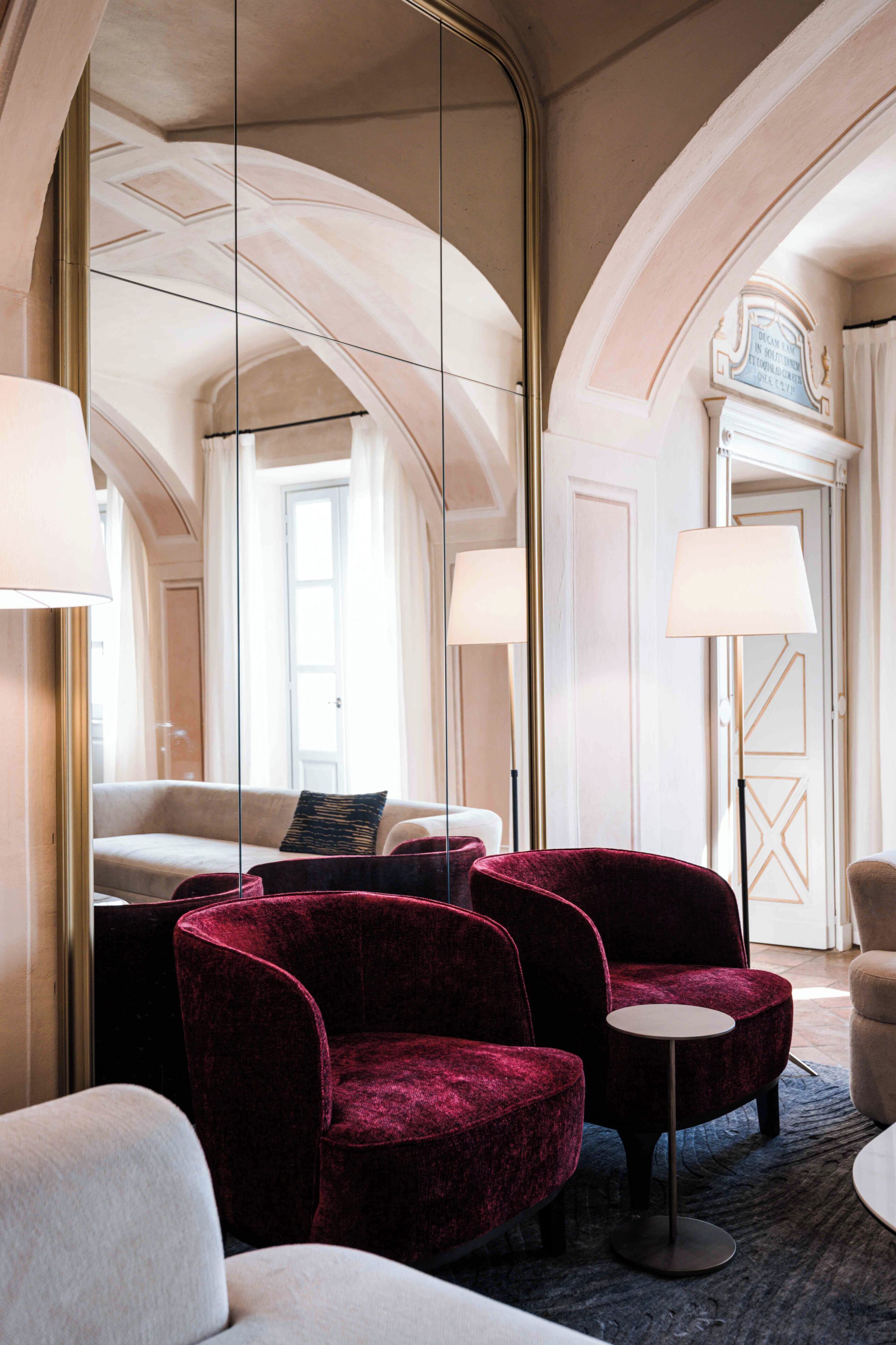 Hotelkamer met een grote spiegel, een bank, twee fauteuils, een klein rond tafeltje en een deur met een bordje.