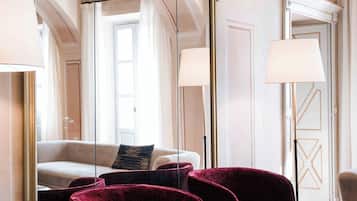 Hotelkamer met een grote spiegel, een bank, twee fauteuils, een klein rond tafeltje en een deur met een bordje.