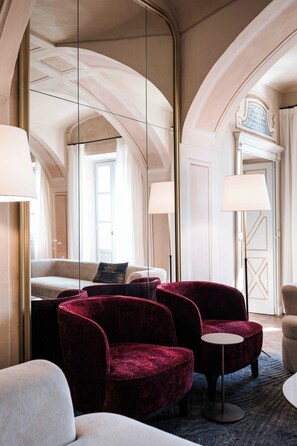 Habitación de hotel con un espejo grande, un sofá, dos sillones, una mesita redonda y una puerta con un cartel.