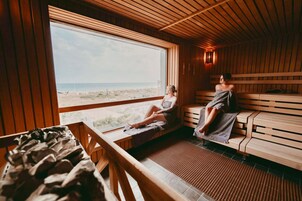 Un sauna con bancos de madera y un ventanal con vista a la playa.