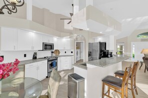 A modern kitchen with white cabinets, stainless steel appliances, and a central island with bar stools. - VRCC Villa Casa del Sol (Cape Coral)
