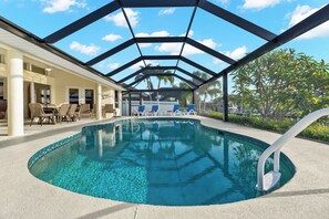 An indoor swimming pool with a glass ceiling, lounge chairs, and a patio area. - VRCC Villa Casa del Sol (Cape Coral)