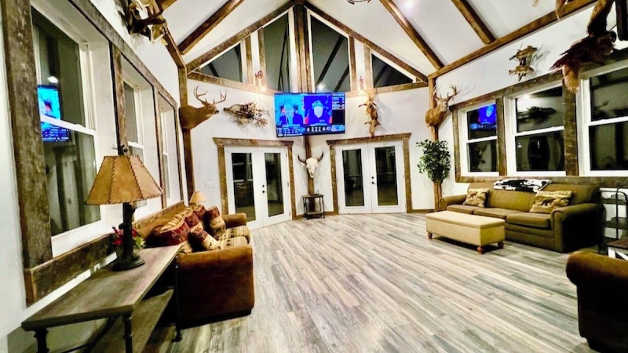 A spacious living room with a high ceiling, wooden beams, a television, and rustic decor including antlers and animal skulls.