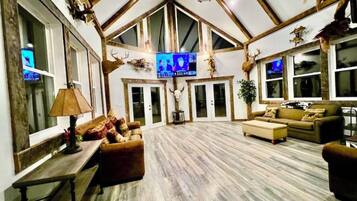 A spacious living room with a high ceiling, wooden beams, a television, and rustic decor including antlers and animal skulls.