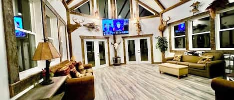 Un salón amplio con techo alto, vigas de madera, televisor y decoración rústica que incluye astas y calaveras de animales.