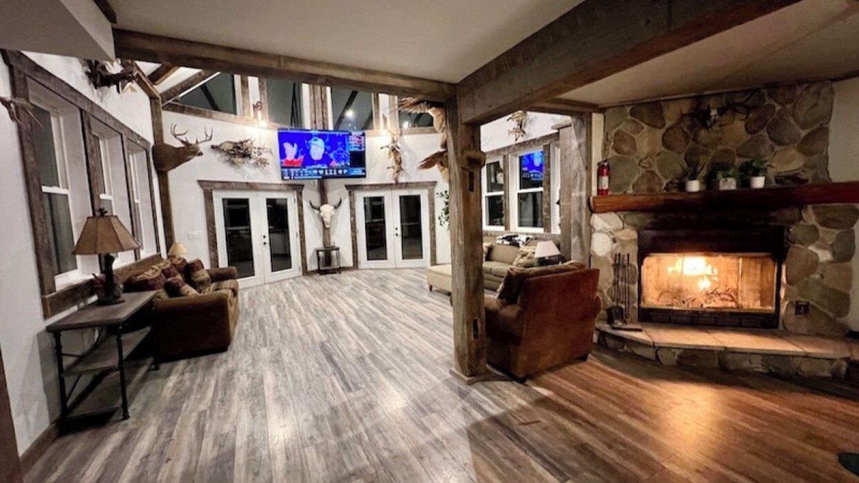 Een ruime woonkamer met een stenen open haard, houten balken en een groot televisiescherm.