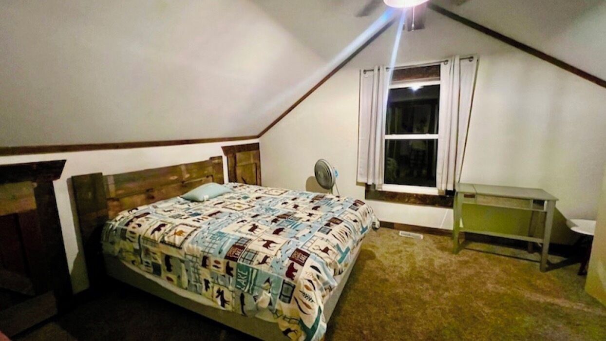 Un dormitorio con cama, ventilador, ventana y escritorio.