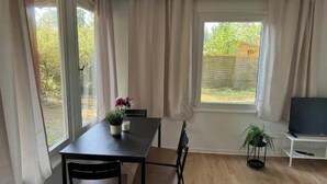 Een eethoek met een tafel, stoelen, een tv op een dressoir en een raam met gordijnen.