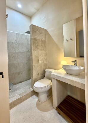 Ein Badezimmer mit Toilette, Waschbecken, Spiegel und Duschbereich.