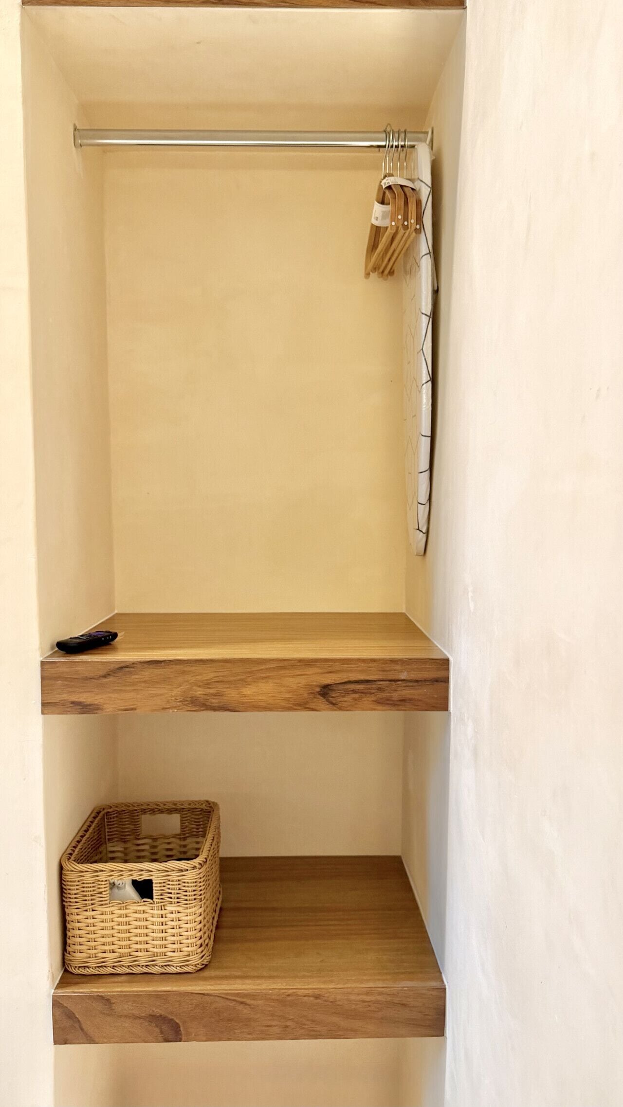 Une pièce avec une étagère en bois, un panier en osier et une tige métallique munie de crochets.