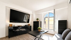 A modern living room with a flat-screen TV, a dining table, a sofa, and a window with a view of buildings. - Joli 2 pi ces Monaco (Monaco)