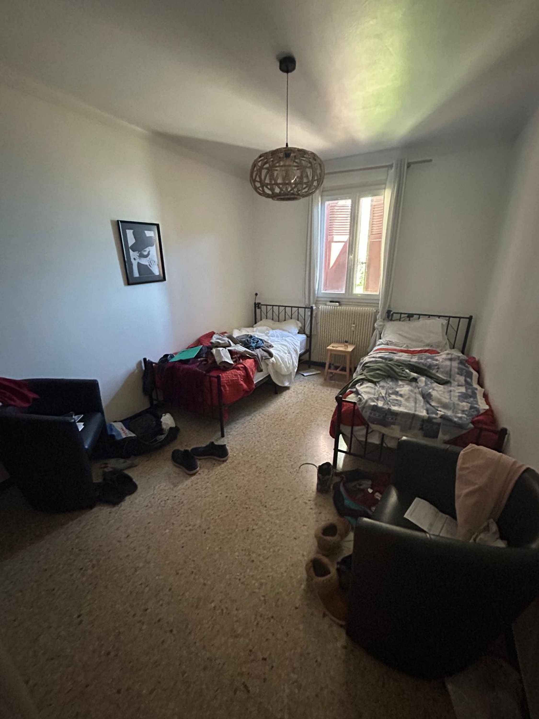 Une petite chambre avec deux lits simples, un radiateur, un luminaire suspendu et un tableau encadré au mur.