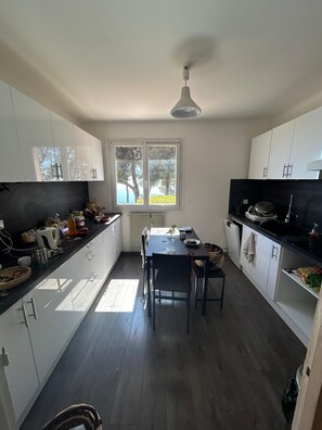 A compact kitchen with white cabinets, a dining table, and a window with a view of trees. - Garden Apartment With Breathtaking Views Over ze (Èze)
