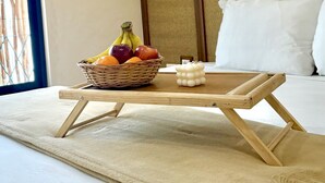 Un lit bien fait, avec une petite table en bois et un panier de fruits.