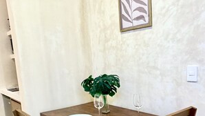 Une table à manger avec quatre chaises en bois, un vase avec une plante et une œuvre d’art représentant une feuille, encadrée, accrochée au mur.