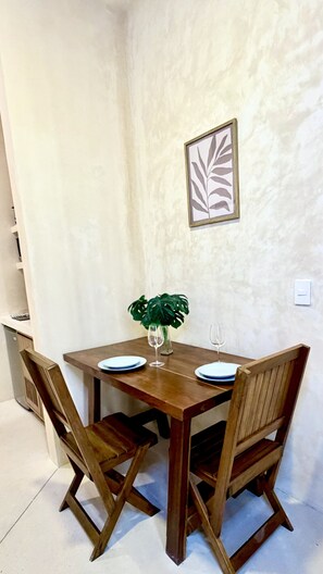 Ein Esstisch mit vier Holzstühlen, eine Vase mit Pflanze und ein gerahmtes Kunstwerk mit einem Blatt an der Wand.