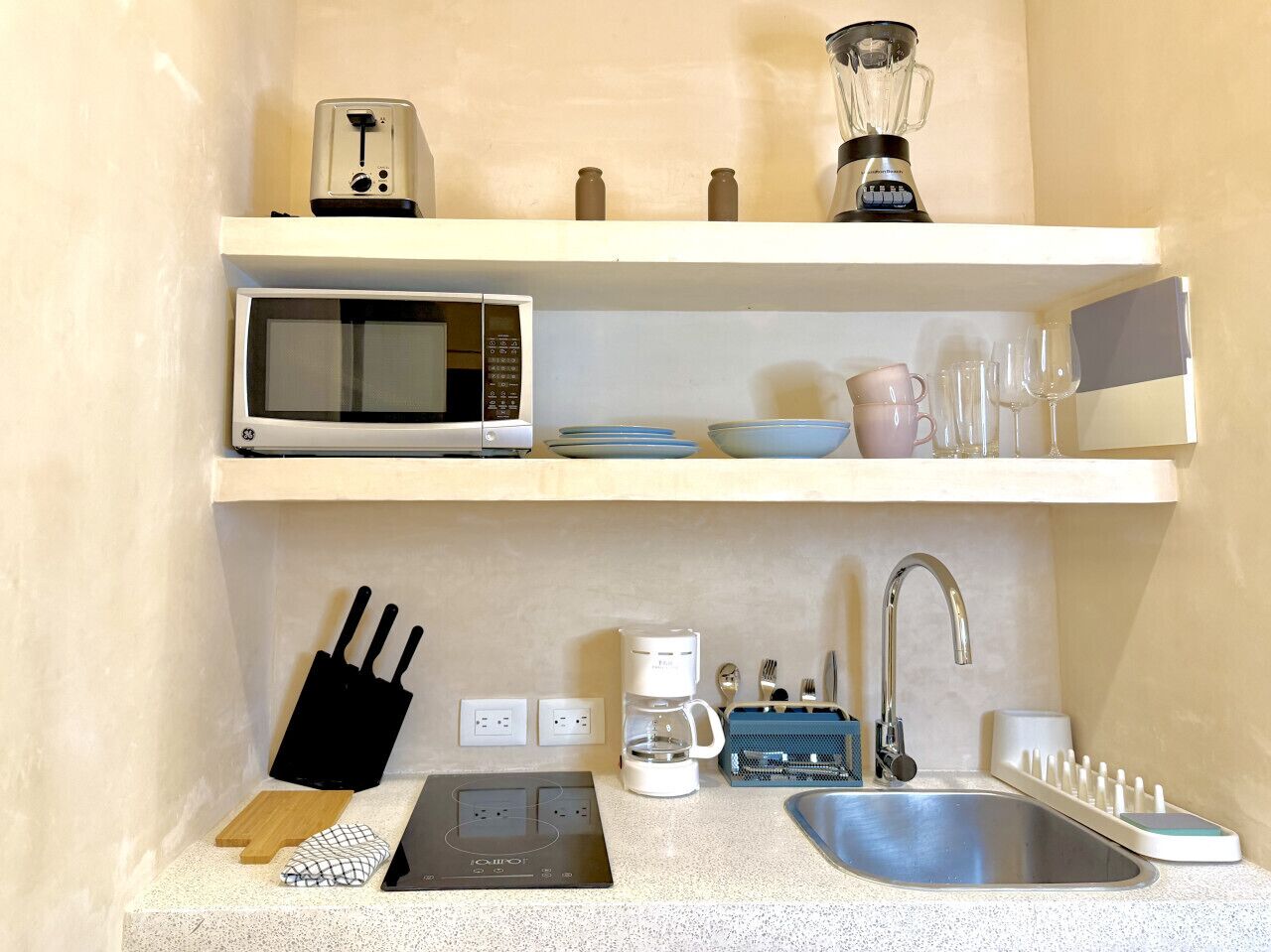 Cocina compacta equipada con microondas, tostadora, licuadora, cafetera y un lavamanos con grifo.