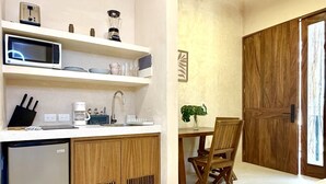 Une cuisine compacte équipée d’un four à micro-ondes, d’une machine à café et d’un petit réfrigérateur. Un coin repas est aménagé avec une table et des chaises en bois.