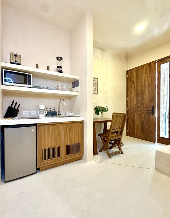 Eine kleine Küche mit Mikrowelle, Kaffeemaschine und kleinem Kühlschrank. Es gibt einen Essbereich mit Holztisch und Stühlen.